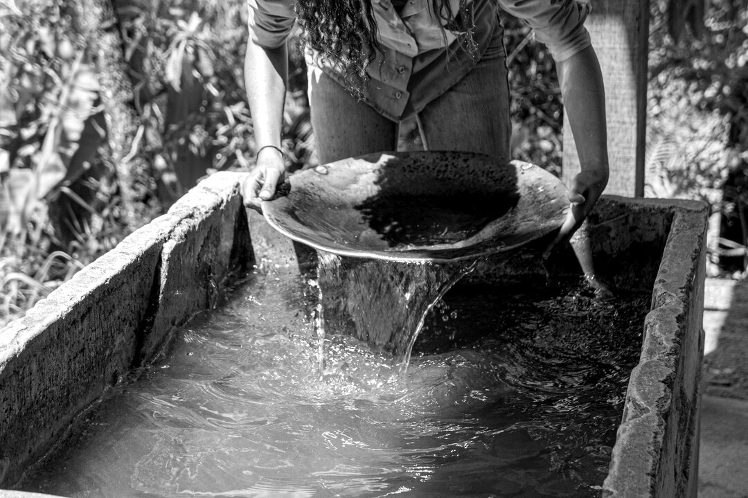 Hands holding a gold pan as water pours back into a stone trough
